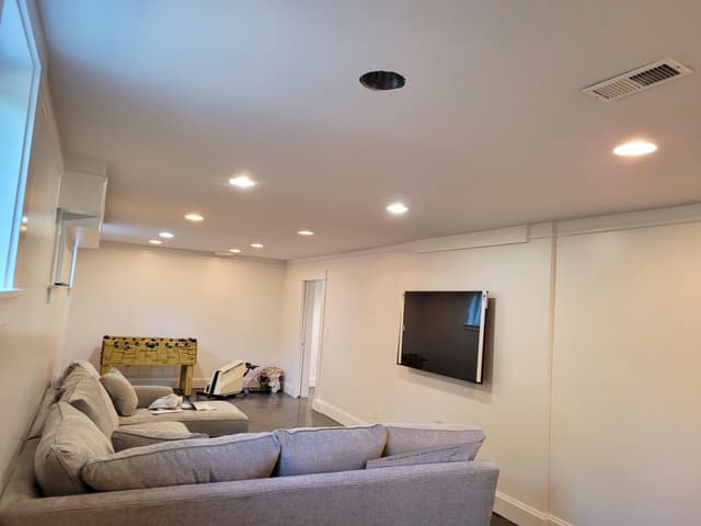 An in-progress photo of a basement rec room with new walls, lighting, and a mounted TV.