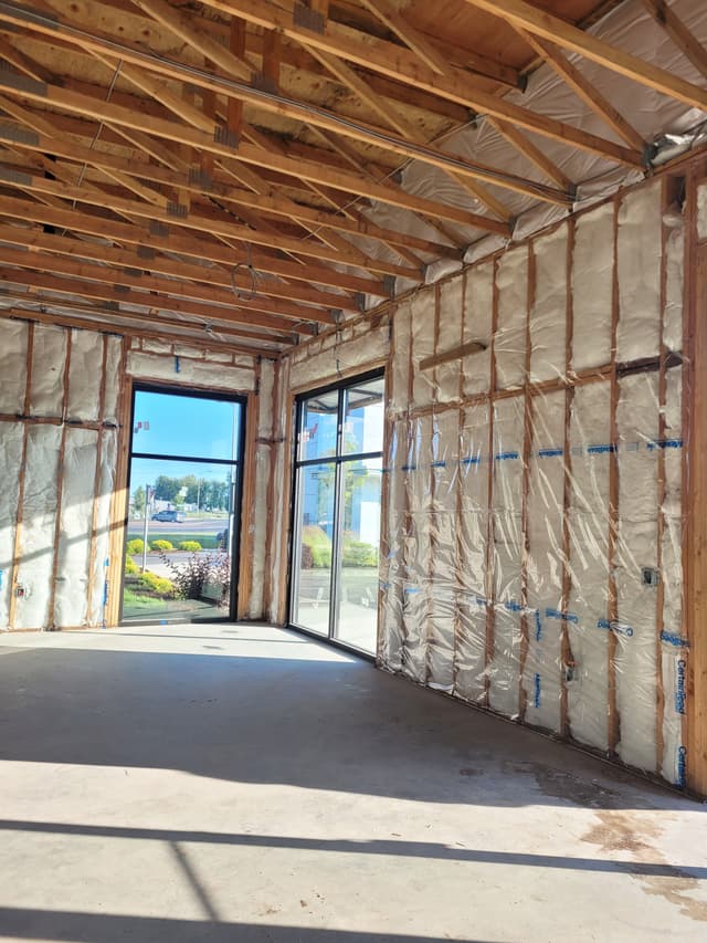 An in-progress photo of a commercial storefront framing buildout. The photo shows the wooden frame and insulation, with large windows and doors installed.