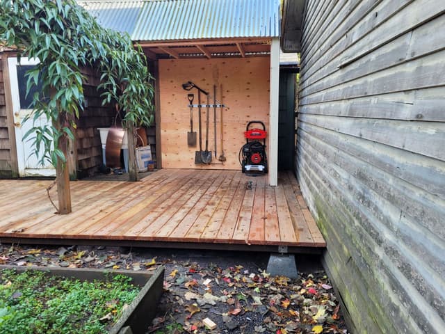 A photo of a covered tool storage area with wooden deck and corrugated metal roof.