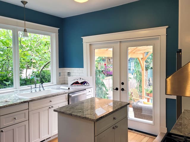 A photo of a kitchen with fresh paint, white cabinets, granite countertops, and a view of the garden through the window.