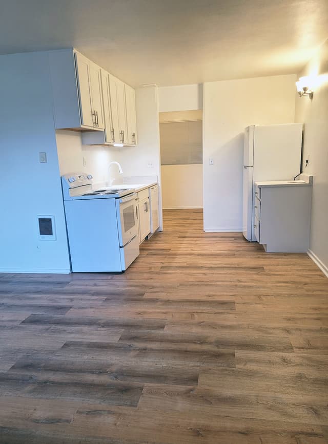 A photo of a newly renovated apartment kitchen with white cabinets and appliances, and wood flooring.