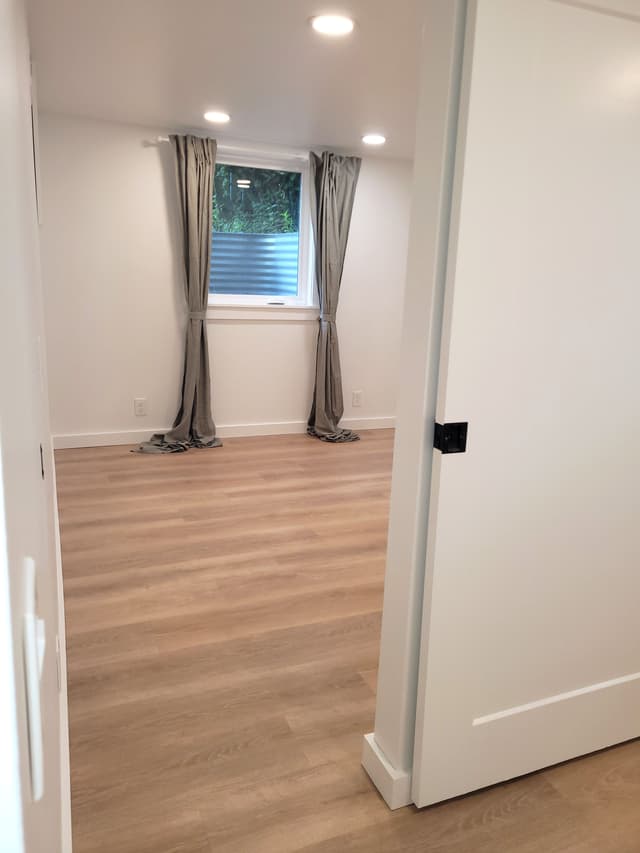 A photo of a new basement bedroom with a sliding barn door, vinyl flooring, and natural light.