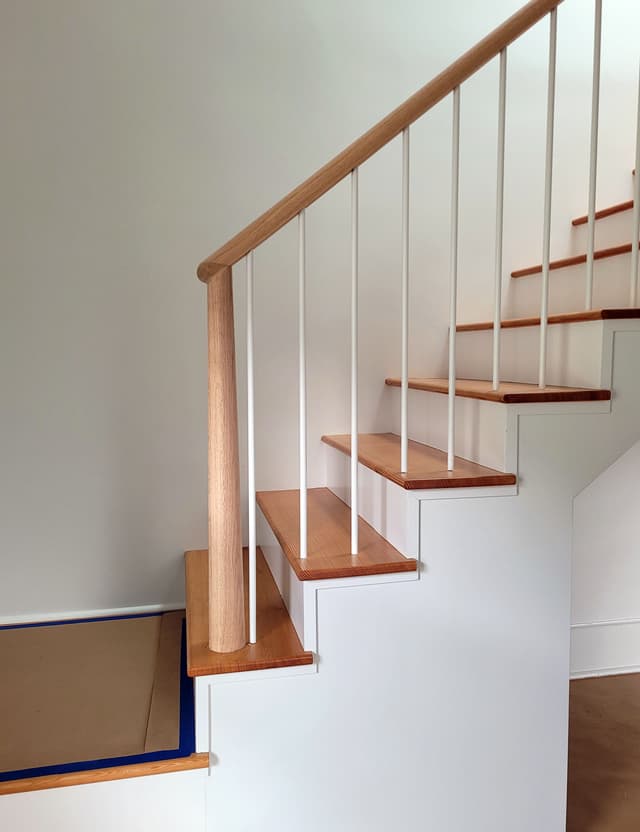 A photo of a newly installed staircase with oak handrail and painted iron balusters.