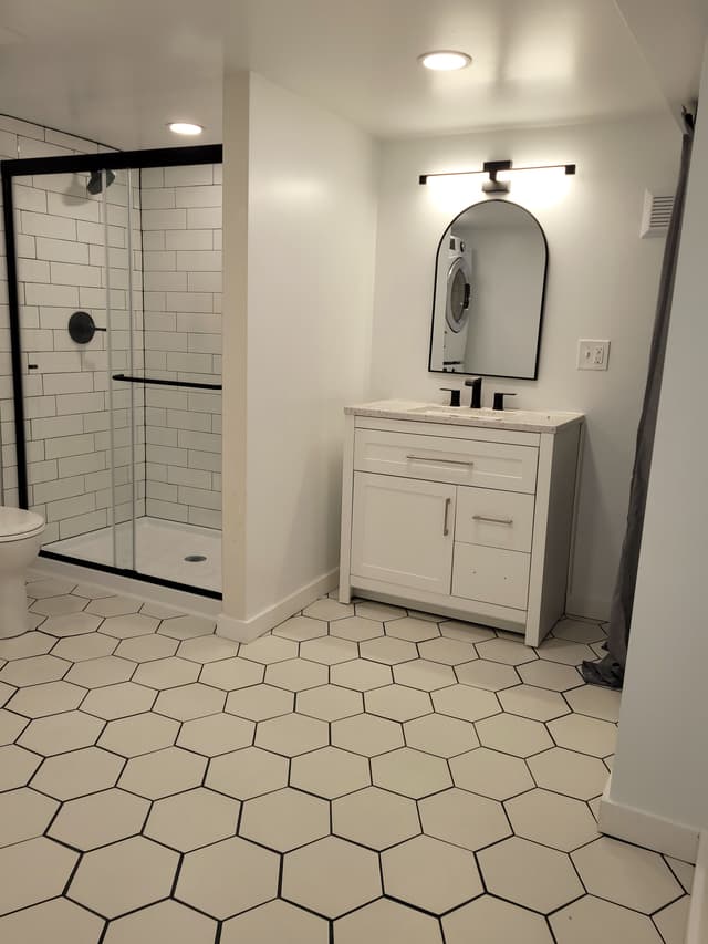 A bathroom with white walls and white hexagonal tiles on the floor. A sliding glass shower door is in the background.