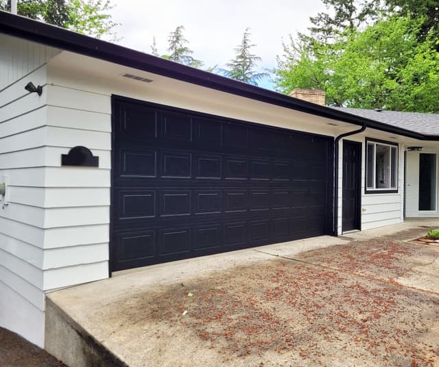 A white garage with a dark blue door and a sloped concrete driveway.