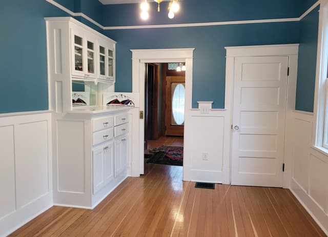 A kitchen with white cabinets, blue walls, and a shiny hardwood floor.