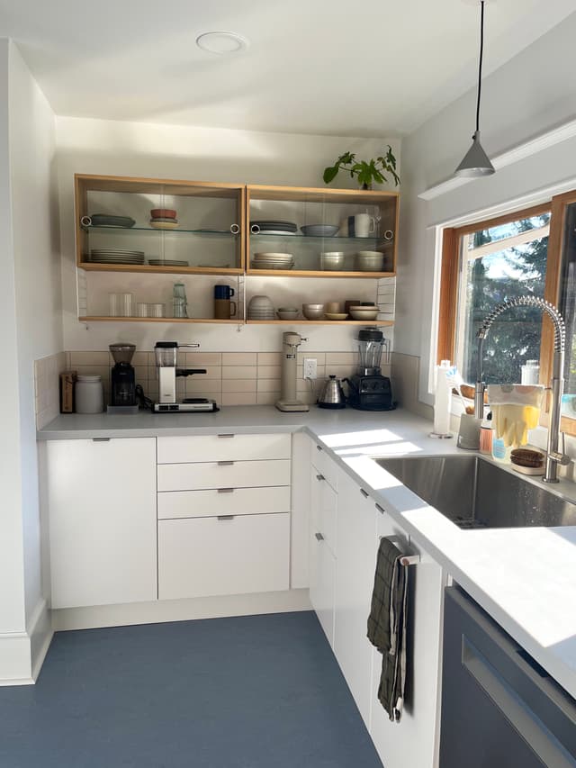 A kitchen with a blue floor, white cabinets, a tile backsplace, and a blonde wood cabinet with glass sliding doors.