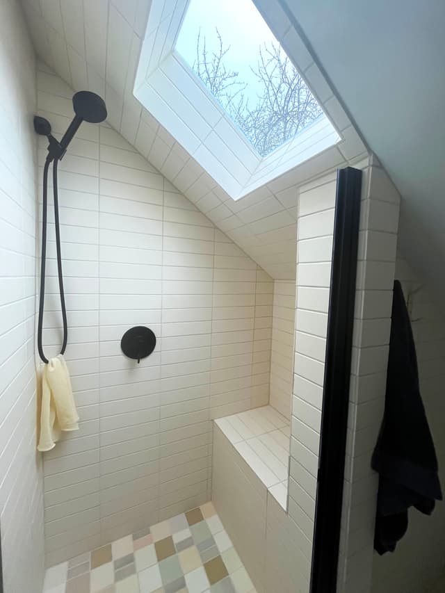 A standing shower with cream-colored rectangular tiles and a skylight.